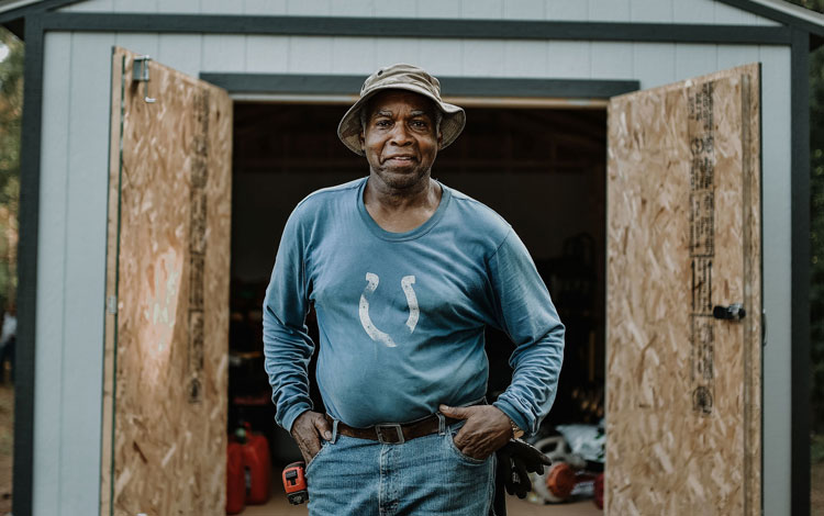 Man with his hands on his hips smiling at camera standing outside his shed. 